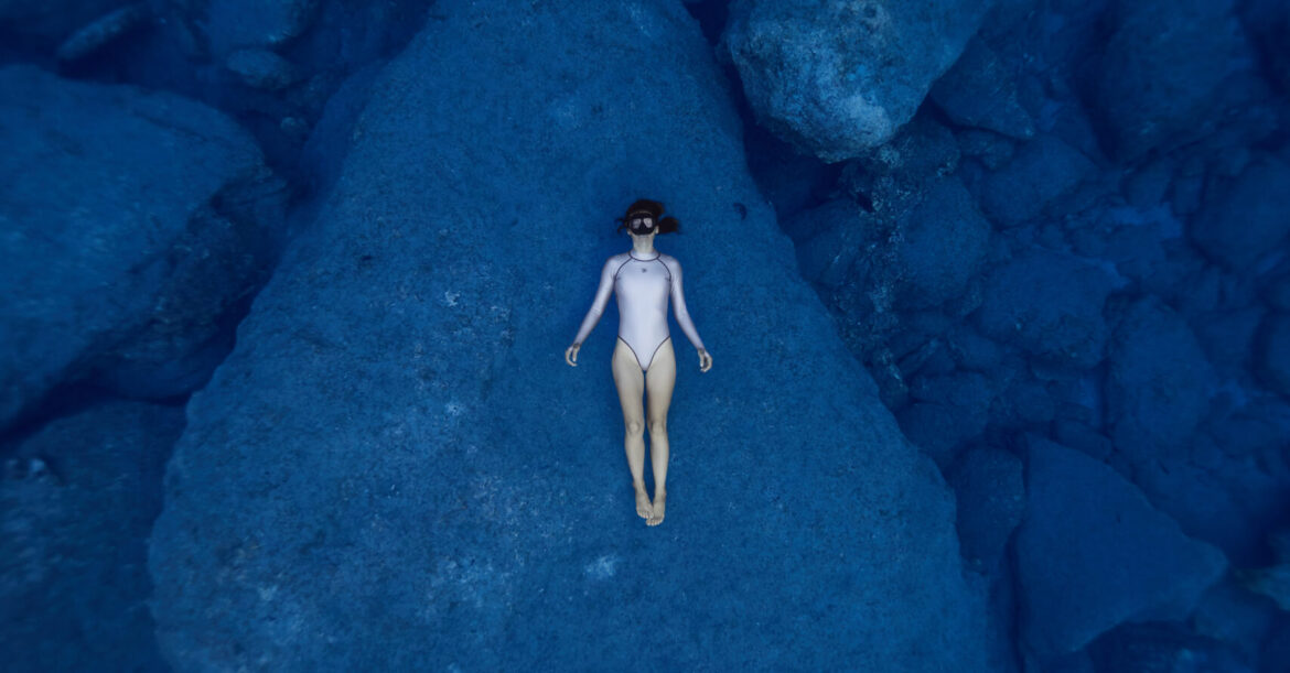a female freediver lying on the bottom of the sea on a big rock